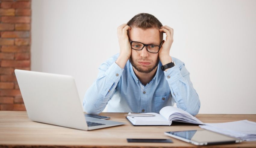 A man sitting at a desk with his hands on his head.