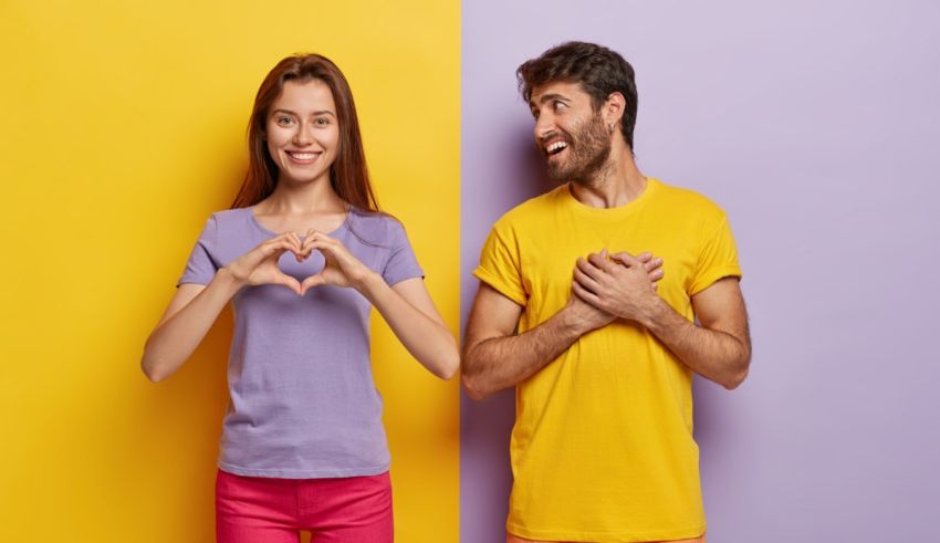 Young man and woman making a heart shape on a yellow and purple background.