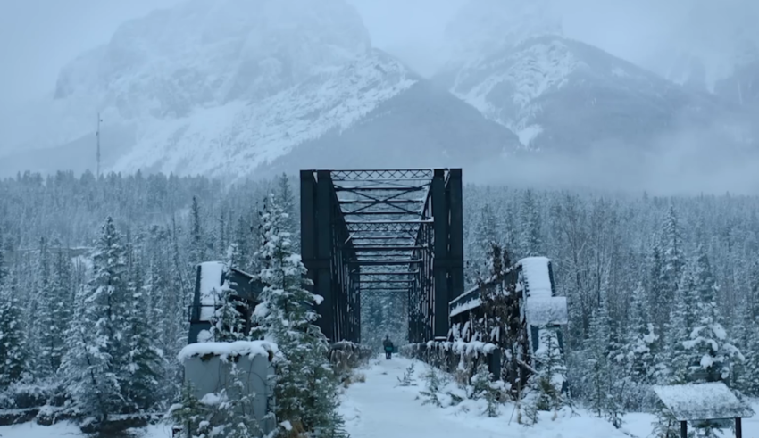 A train bridge in the snow with mountains in the background.