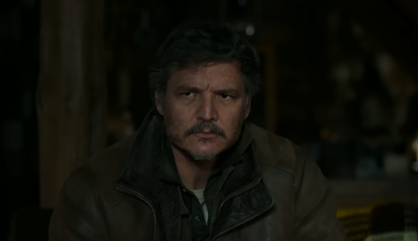 A man in a brown jacket sitting in a dark room.