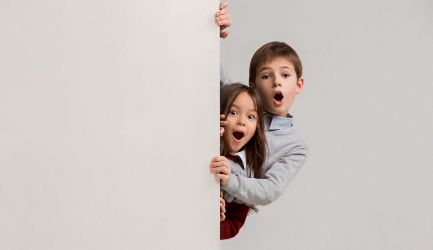 Two children peeking out of a white wall.