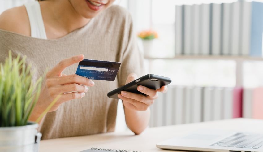 A woman holding a credit card in front of a laptop.