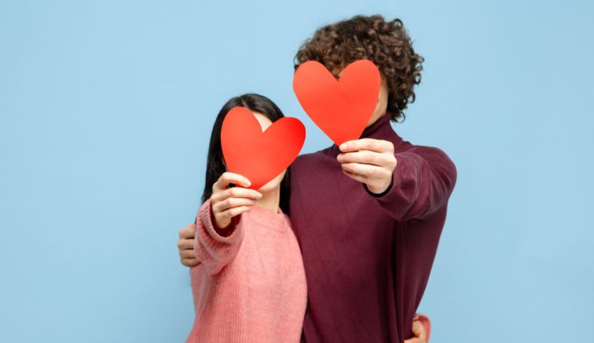 Young couple holding red heart shaped paper over blue background.