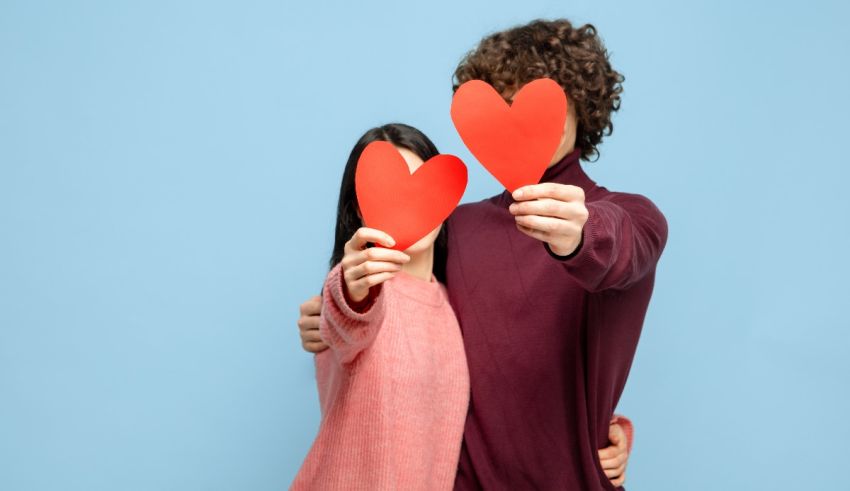 Young couple holding red heart paper over blue background.