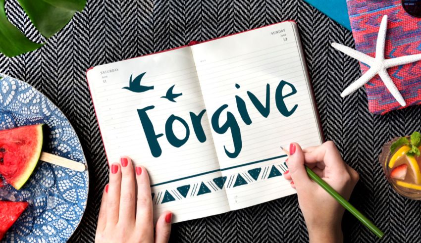 A hand writing the word forgive on a notebook.