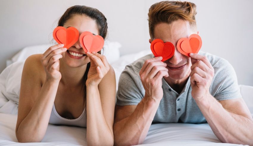 A man and a woman are lying on a bed with red hearts in their eyes.