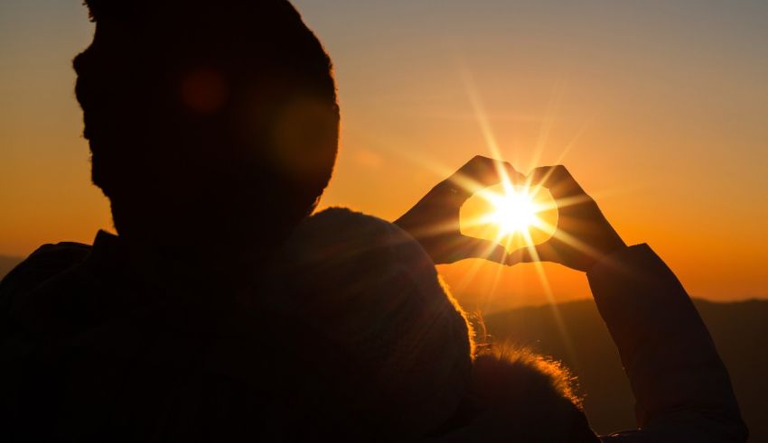 A couple making a heart shape with their hands at sunset.