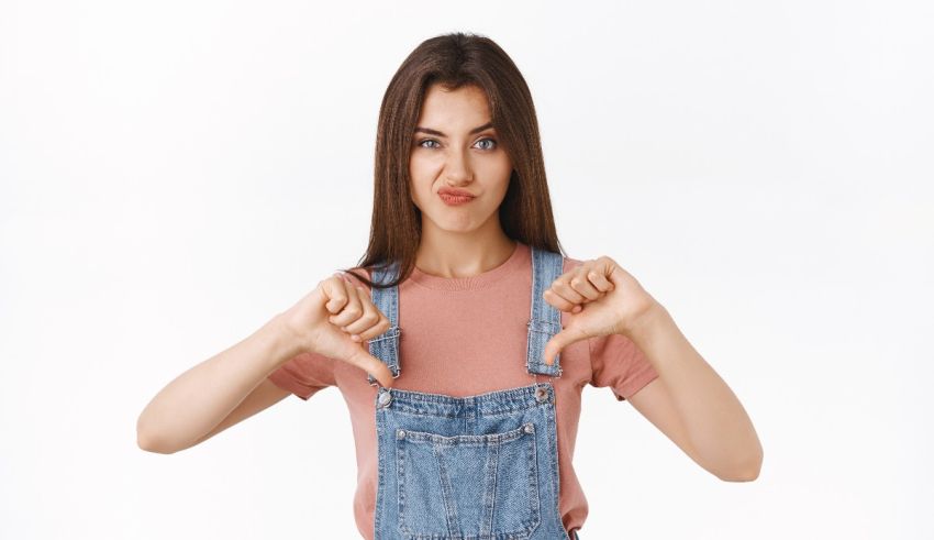 A girl in overalls making a thumbs down gesture.