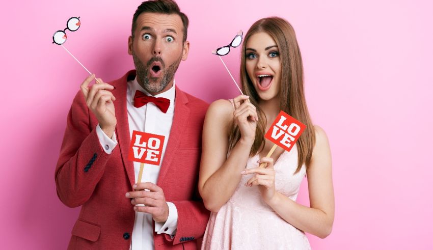 A man and woman posing for a photo with a love sign on a pink background.