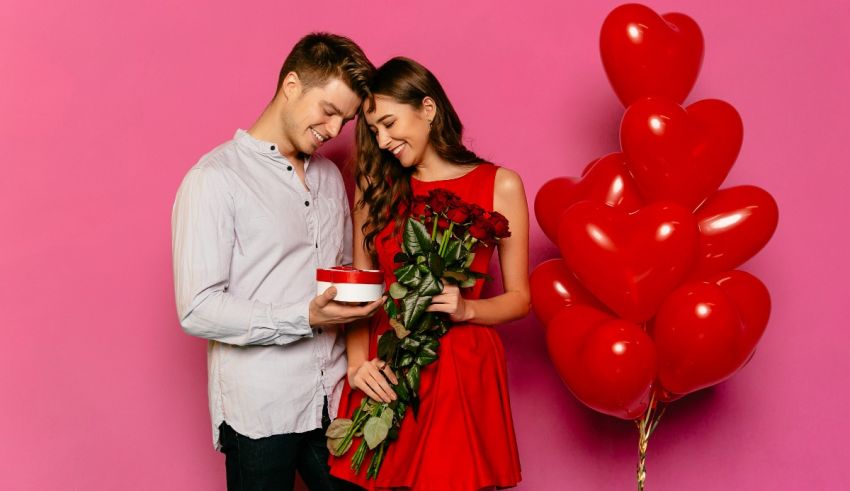 A man and woman holding a bouquet of red roses on a pink background.
