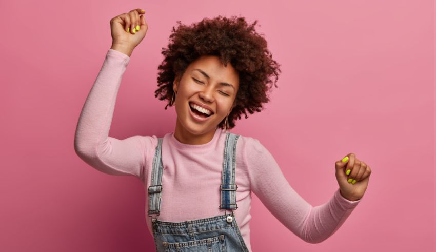 Afro-american woman in overalls dancing on a pink background.