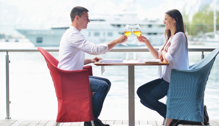 A man and woman toasting wine at a table on a dock.
