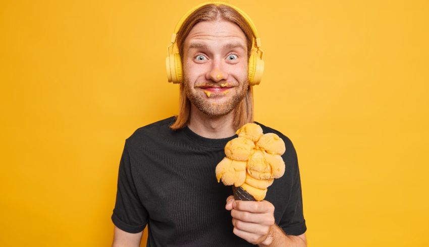 A man with headphones holding an ice cream on a yellow background.
