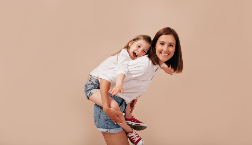A woman is carrying her daughter on her shoulders on a beige background.