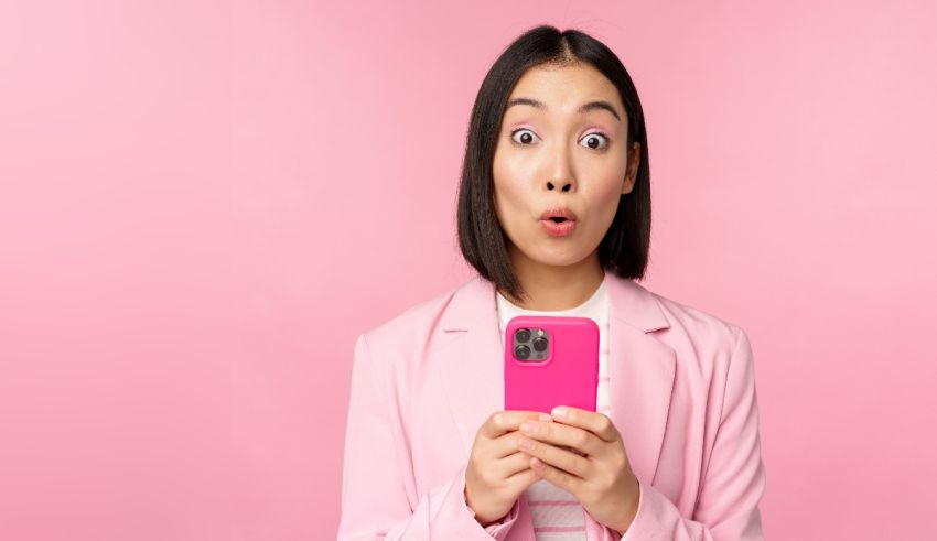 A woman holding a pink phone with a surprised expression.