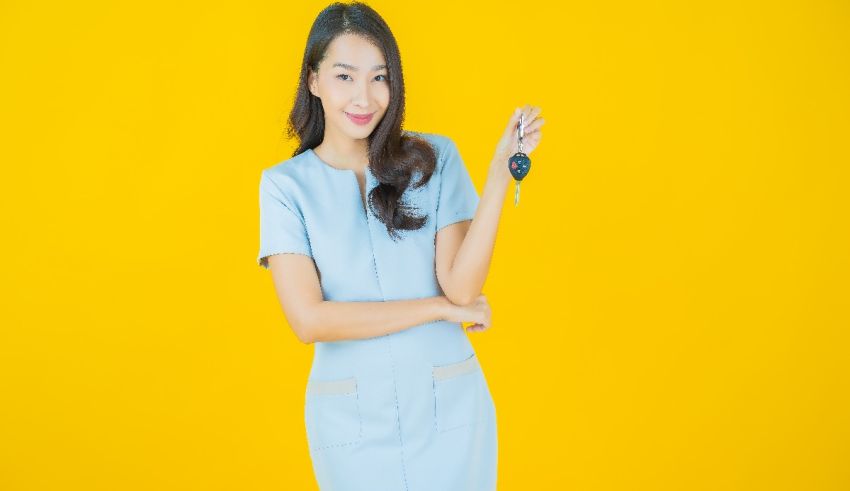 Asian woman holding a car key on a yellow background.