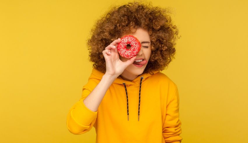 A young woman with curly hair holding a donut on a yellow background.