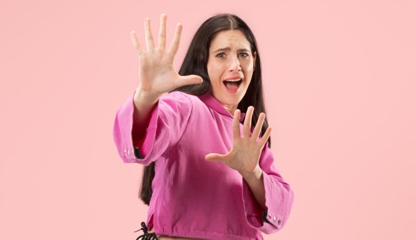 A woman is making a hand gesture on a pink background.