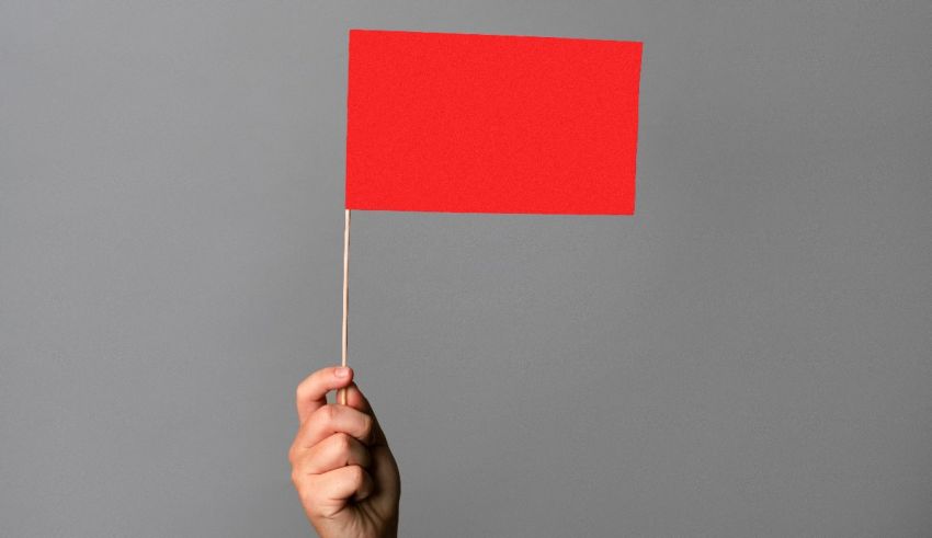 A hand holding a red flag on a gray background.