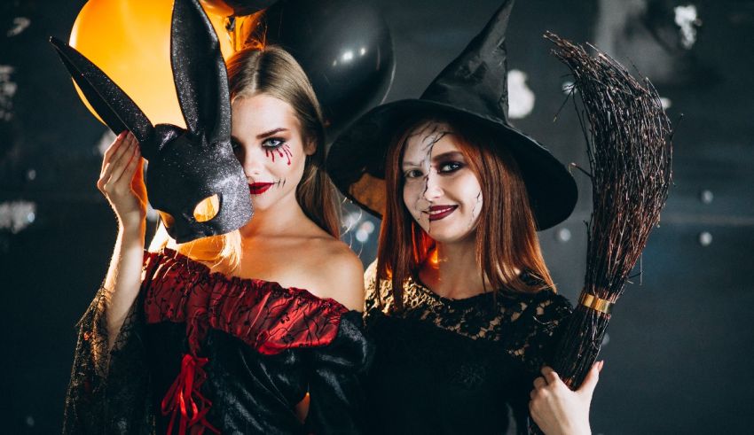 Two women dressed as witches holding brooms and balloons.