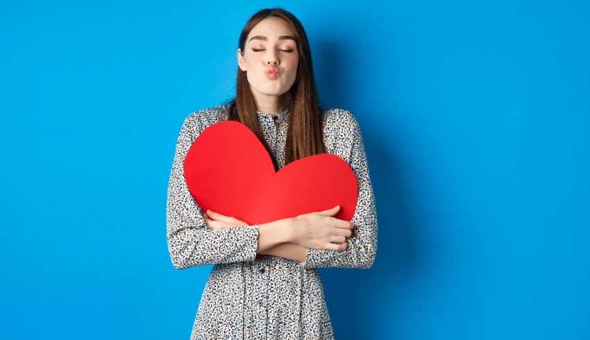 A young woman holding a red heart against a blue background.