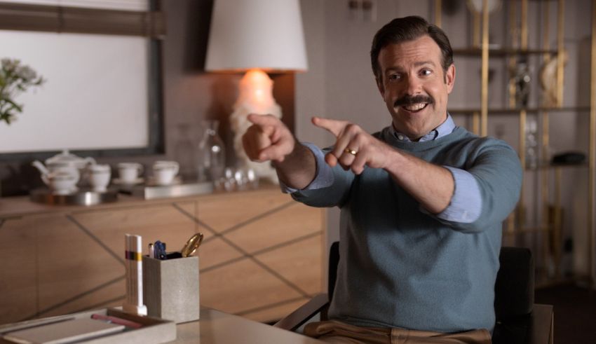 A man sitting at a table with a mustache pointing at something.