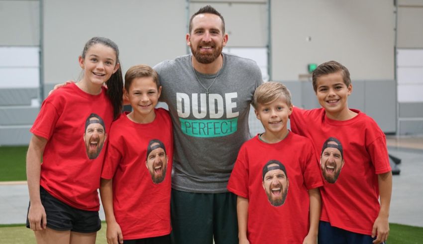 A man with a t - shirt posing with a group of kids.