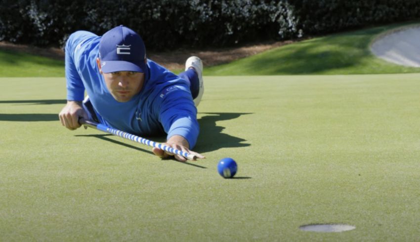 A man is laying down on a golf course with a putter.