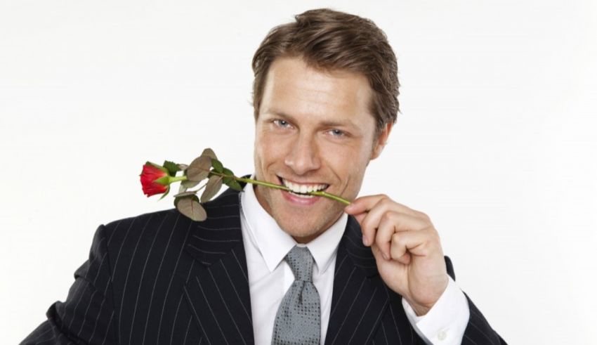A man in a suit with a rose in his mouth.