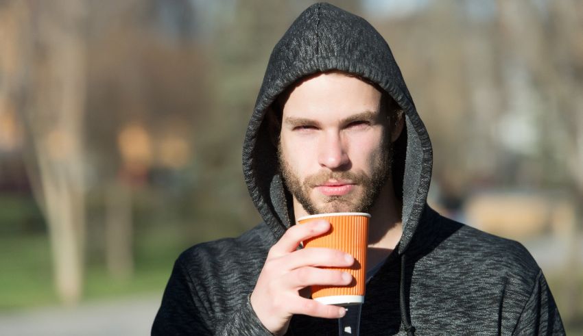 A man in a hoodie drinking a cup of coffee.