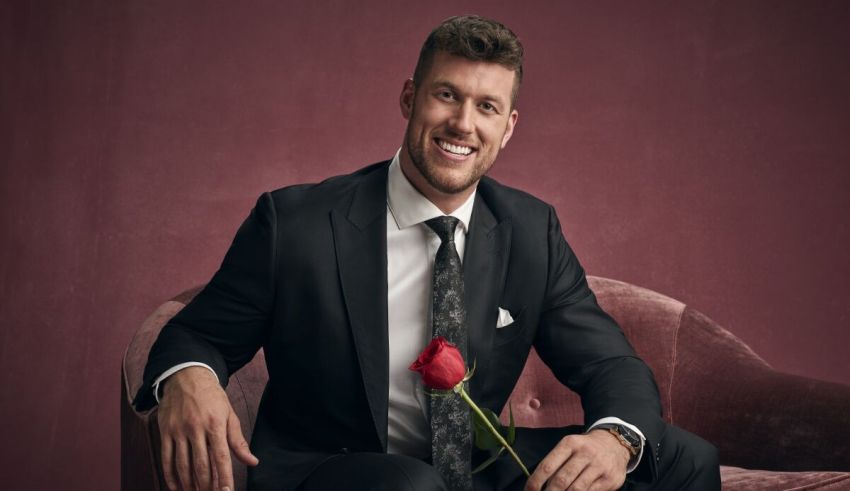 A man in a suit sitting on a couch with a rose.