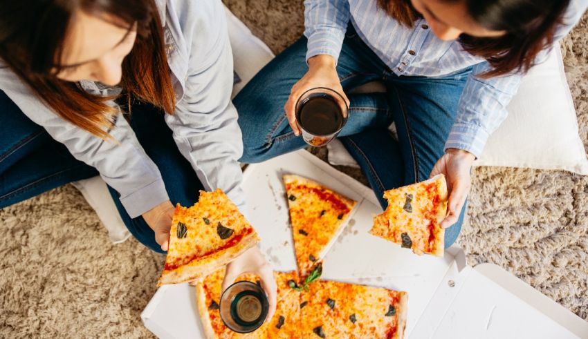 Two women sitting on the floor eating pizza.