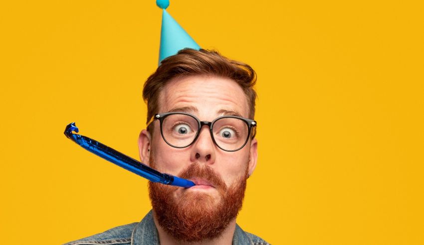 A man with glasses and a party hat is blowing bubbles.