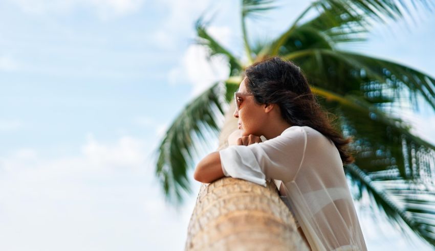 A woman is leaning against a palm tree.