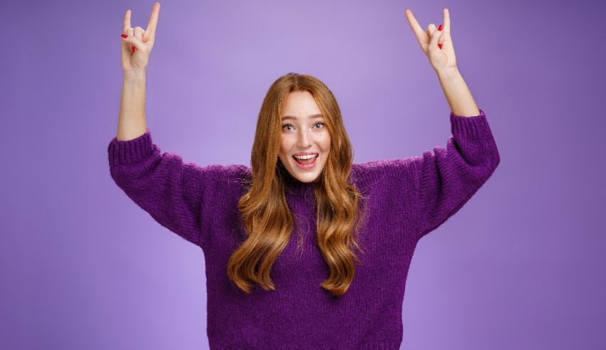 A young woman in a purple sweater is making a rock gesture.