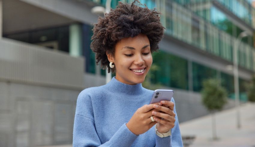 A young african american woman is smiling while using her cell phone.