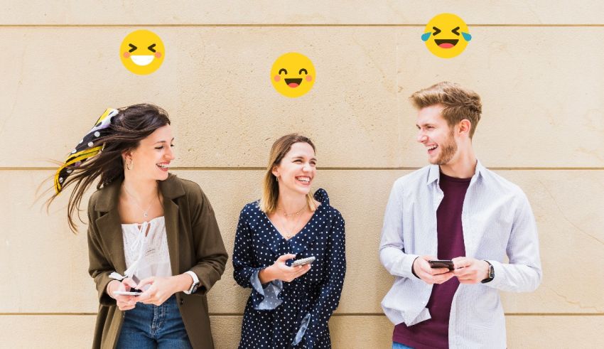 A group of people standing next to a wall with emojis on their phones.
