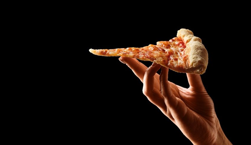 A hand holding a slice of pizza on a black background.