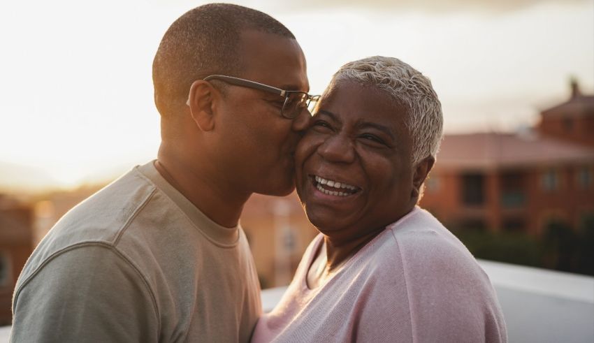 A black man and woman kissing in front of a building at sunset.