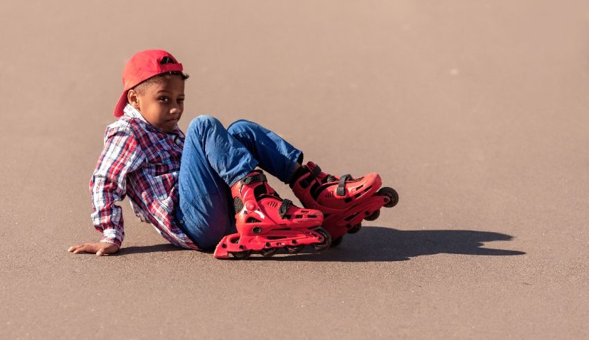 A young boy on roller skates sitting on the ground.