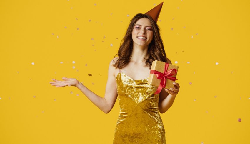 A woman in a gold dress holding a gift on a yellow background.