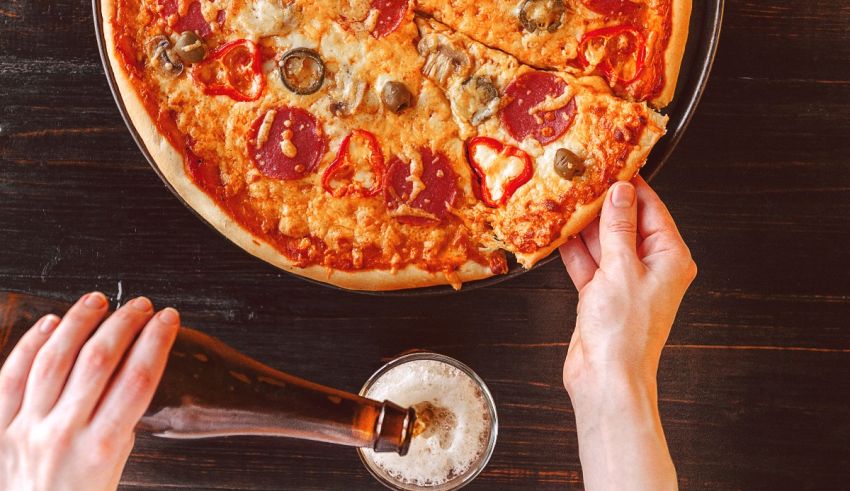 A person is holding a pizza and a beer.