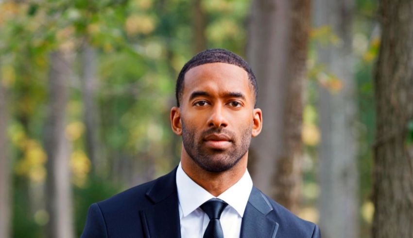 A black man in a suit standing in a wooded area.
