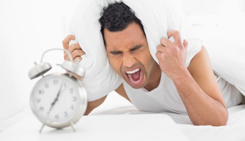 A man waking up in bed with an alarm clock.