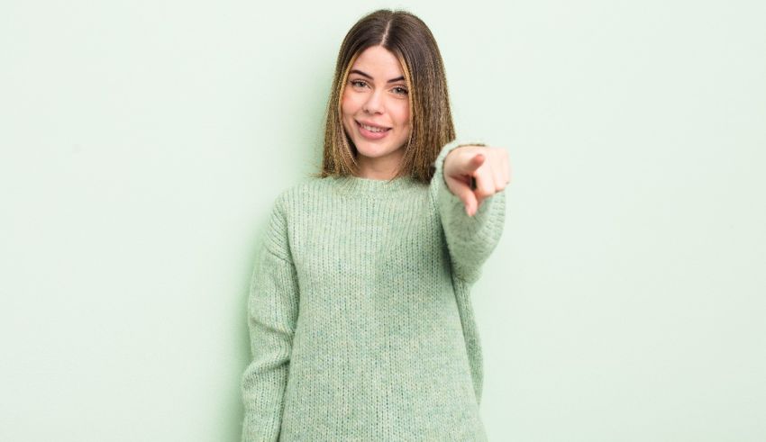 A young woman pointing her finger at the camera on a green background.