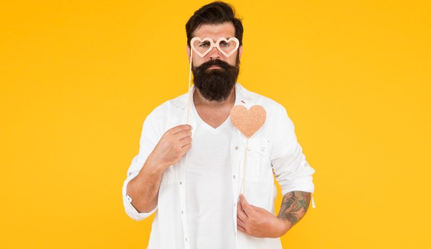 A man with a beard holding a heart on a yellow background.