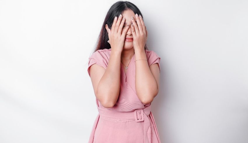 Asian woman covering her eyes with hands on white background.