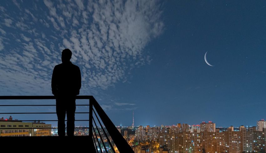 A silhouette of a man standing on a balcony overlooking a city at night.