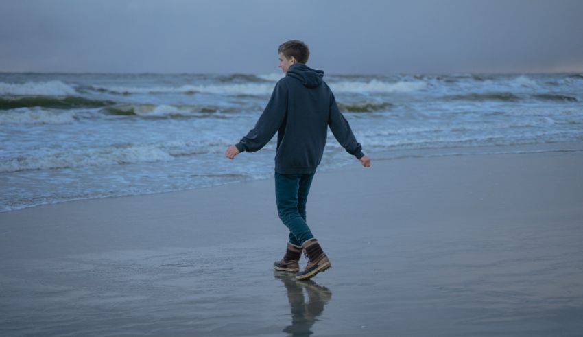 A young man walking along the beach on a cloudy day.