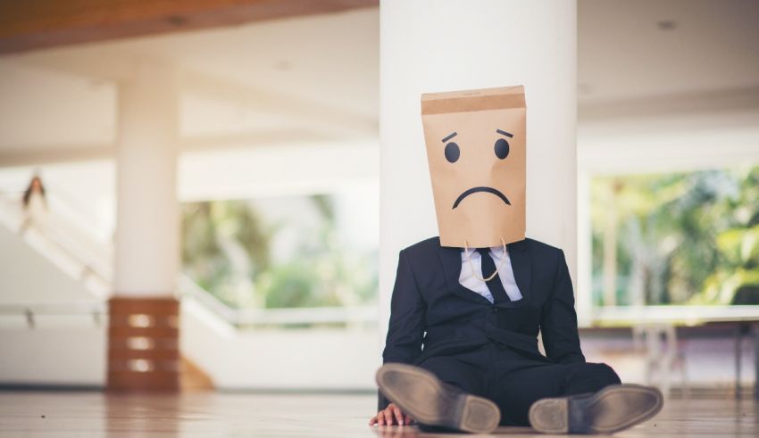 A businessman sitting on the floor with a paper bag on his head.
